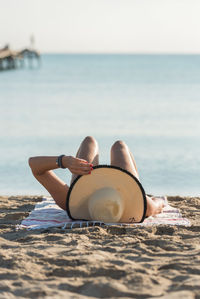 Anonymous female in straw hat lying on sandy seashore in morning and sunbathing during summer holiday on playa de muro