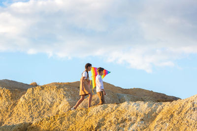 Children boy and girl with kite in their hands climb a high mountain.