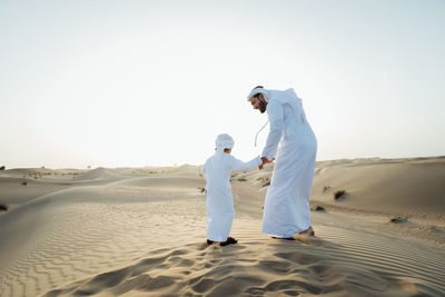 Rear view of men standing on sand against sky