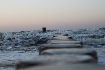 Wooden posts in sea against sky during sunset