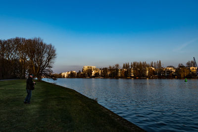 Rear view of man standing by river against clear sky