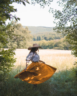 Happy woman dancing in the field wearing hat and dress