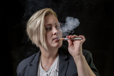 Portrait of young woman smoking cigarette against black background