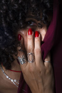 Close-up portrait of woman with red transparent cloth on her face against black background. 