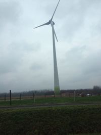 Wind turbines on field against cloudy sky