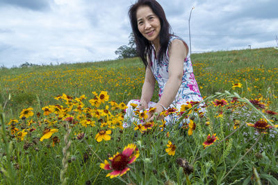 Beautiful young woman standing on yellow flowering field against sky