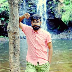 Portrait of young man standing against waterfall