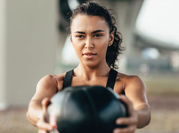 Smiling young woman exercising with ball while standing outdoors