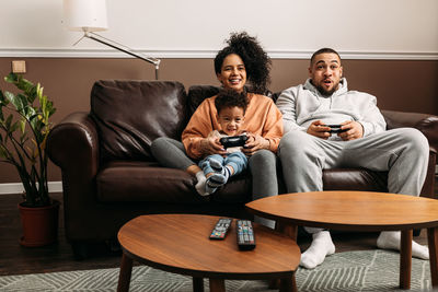 Mother and father with son playing video game while sitting on sofa at table