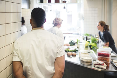 Rear view of male chef standing by wall with female colleagues working in kitchen at restaurant