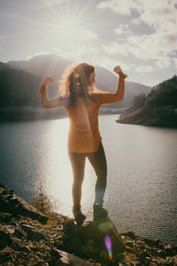 Full length of young woman standing by lake against sky