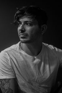 Portrait of young man looking away against black background