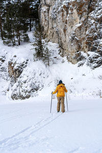 Rear view of young woman in yellow clothes with backpack skiing near mountain  winter sports hiking