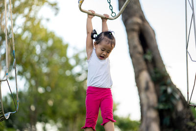 Girl playing on monkey bar in playground against sky