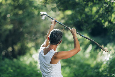 Rear view of man with arms raised standing against plants