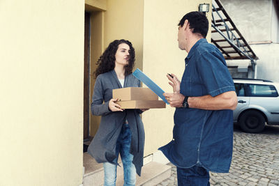 Woman and delivery man talking against house