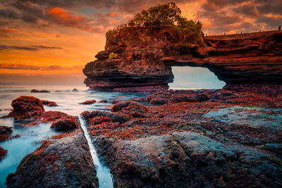 Rock formation on beach against sky during sunset