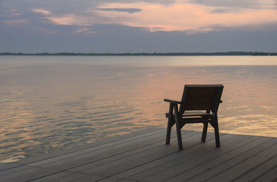 Chair on beach against sky during sunset