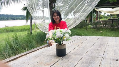 Portrait of smiling woman standing by railing against plants