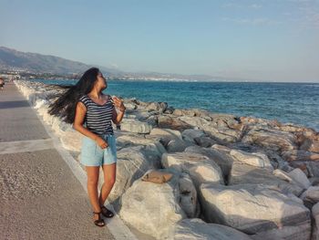 Full length of woman standing on walkway by sea against sky