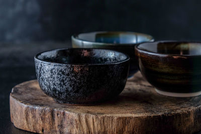 Close-up of black bowls on tree stump against black background