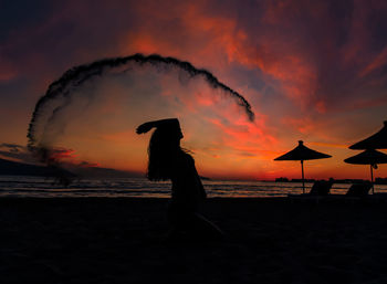 Silhouette woman standing at beach against sky during sunset