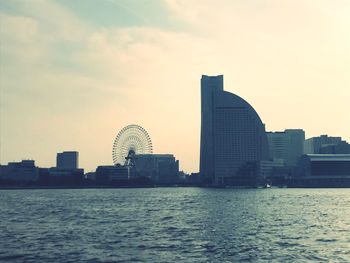 Sea by modern buildings against sky during sunset