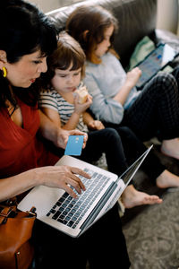 High angle view of woman doing online shopping through laptop while sitting with daughters at home