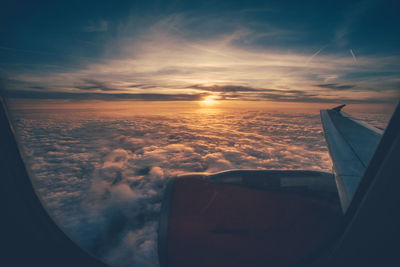 Cropped image of airplane flying over cloudscape against sky seen through window