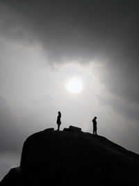 Silhouette people standing on rock against sky