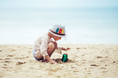 Rear view of boy sitting at beach against sky