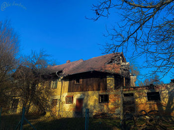 Abandoned house and bare trees against blue sky