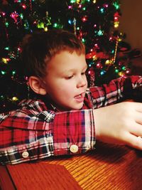 Close-up of boy sitting against christmas tree