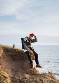 Man sitting on rock against sky