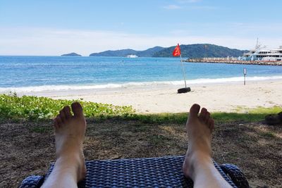 Low section of man relaxing on beach against sky