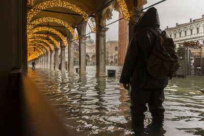 Rear view of man standing on water by buildings in city