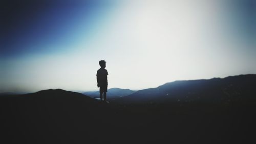 Silhouette boy standing on mountain against clear sky