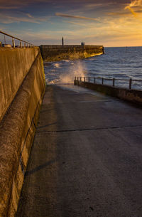 Footpath by sea against sky during sunset