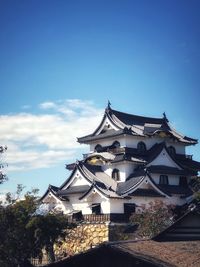 Traditional building by trees against blue sky