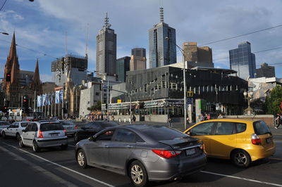 Cars on road by buildings in city against sky