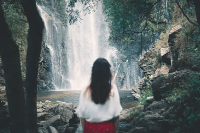 Rear view of woman standing against waterfall