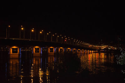 Illuminated bridge over river against sky at night