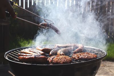 Cropped hand roasting sausage over barbecue grill