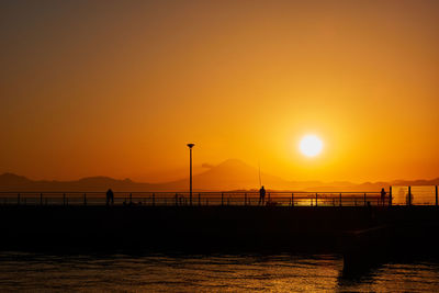Silhouette bridge over sea against romantic sky at sunset
