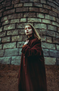 Young woman looking away against brick wall