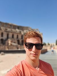 Portrait of young man wearing sunglasses standing against old ruins