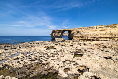 Rock formation by sea against blue sky