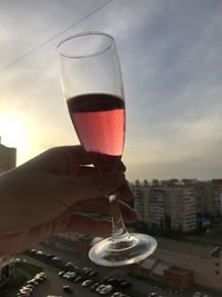 Cropped hand holding drink against sky