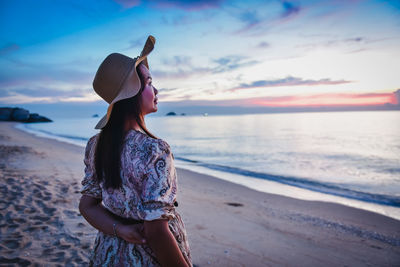 Woman standing at beach against sky during sunset