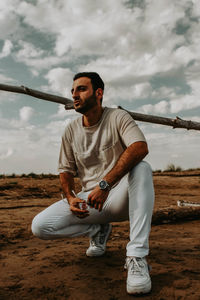 Full length of young man crouching on land against sky